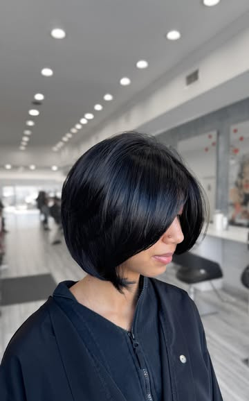 A sharp chin-length bob on blue-black hair, longer at the front, with a long side-swept fringe.